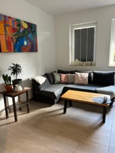Wohnbereich der Ferienwohnung mit bequemer Ausziehcoutch, Couchtisch aus Holz und Bild an der Wand.