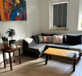 Wohnbereich der Ferienwohnung mit bequemer Ausziehcoutch, Couchtisch aus Holz und Bild an der Wand.