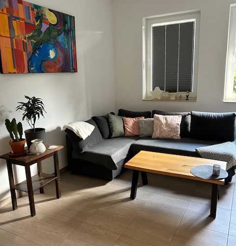 Wohnbereich der Ferienwohnung mit bequemer Ausziehcoutch, Couchtisch aus Holz und Bild an der Wand.