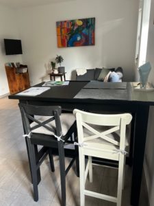 Wohnbereich der Ferienwohnung mit schwarzen Bartisch und Barstühlen, grauen Sofa, Fernseher und farbigen Bild an der Wand