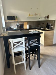 Hellbraune Küchenzeile in der Ferienwohnung mit schwarzen Bartisch und Barstühlen.