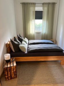 Braunes Bett mit grauer Bettwäsche und Fenster mit grünen Gardinen