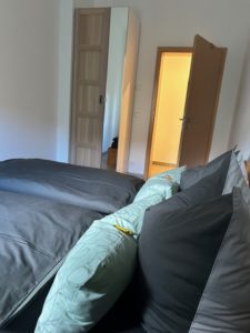 Bett mit grauer Bettwäsche und braunem Kleiderschrank mit Spiegel im Schlafzimmer der Ferienwohnung
