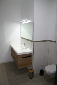 Brauner Waschtisch mit beleuchteten Spiegel im Badezimmer der Ferienwohnung